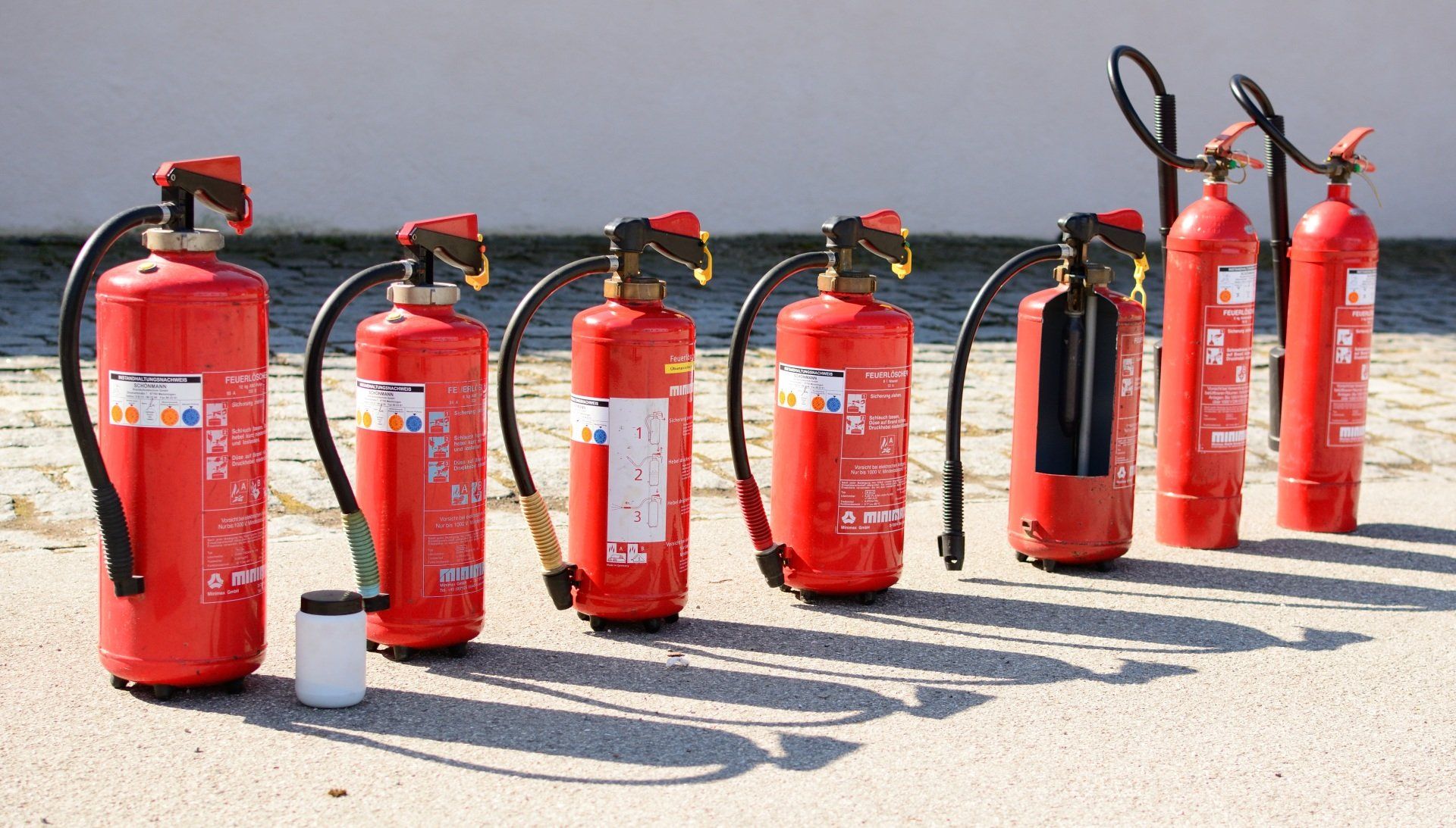 Mehrere rote Feuerlöscher standen im Freien auf einem sonnigen Gehweg in der Nähe einer Mauer.