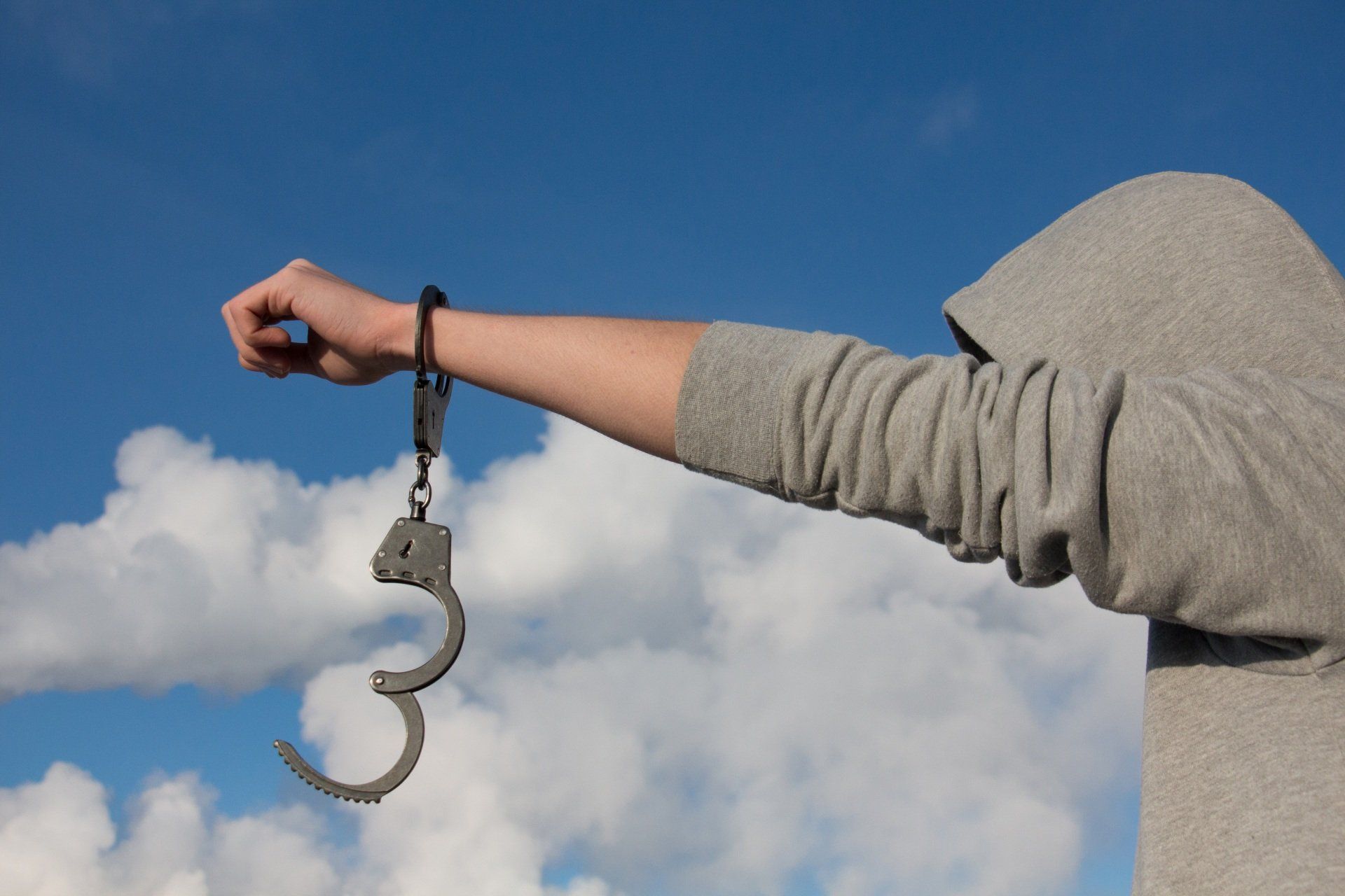 Eine Person in grauem Ärmel hält eine zerbrochene Handschelle vor einem blauen Himmel mit Wolken.