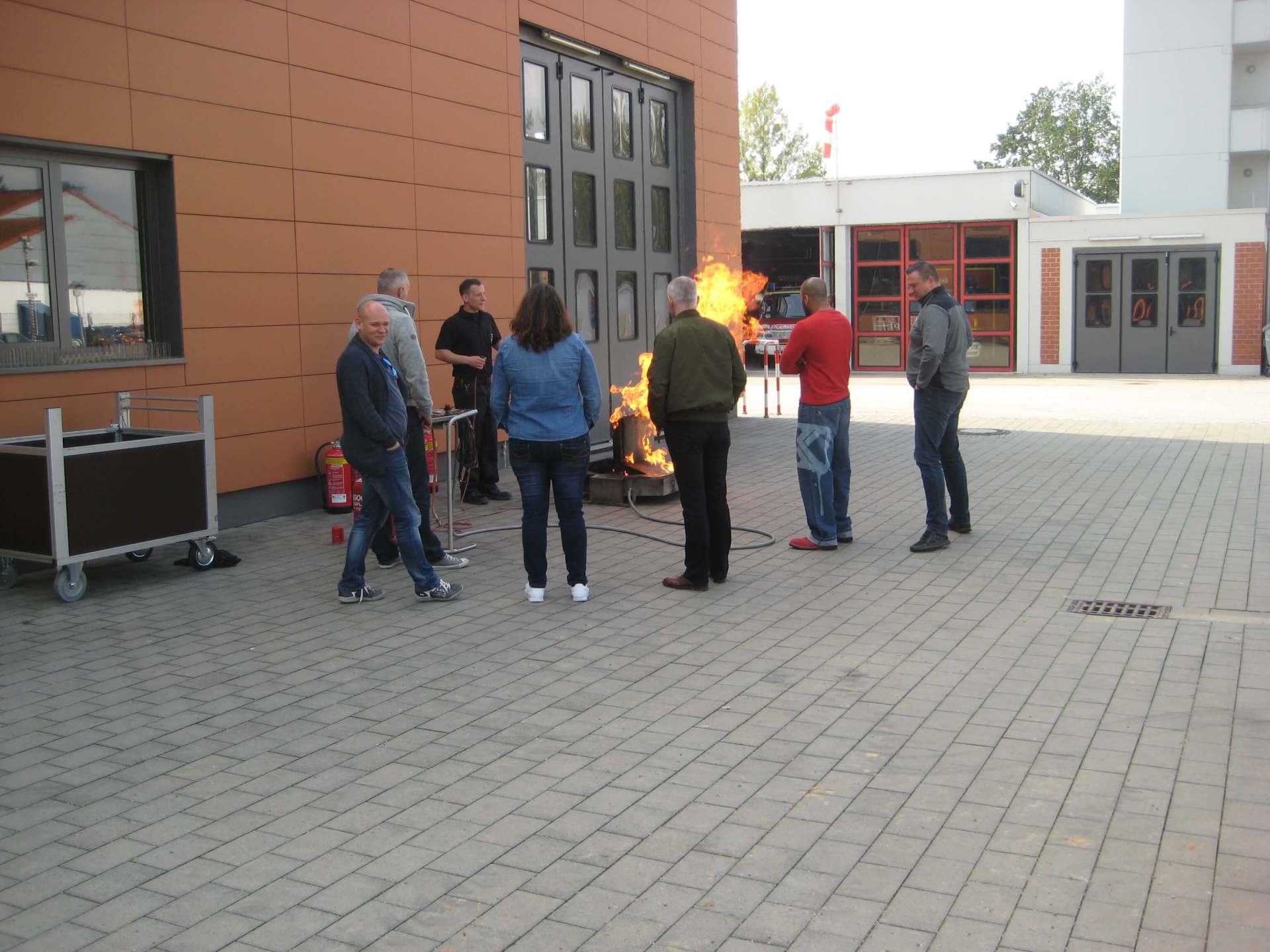 Menschen stehen in der Nähe eines kleinen Feuers in einem gepflasterten Innenhof neben einem Backsteingebäude.