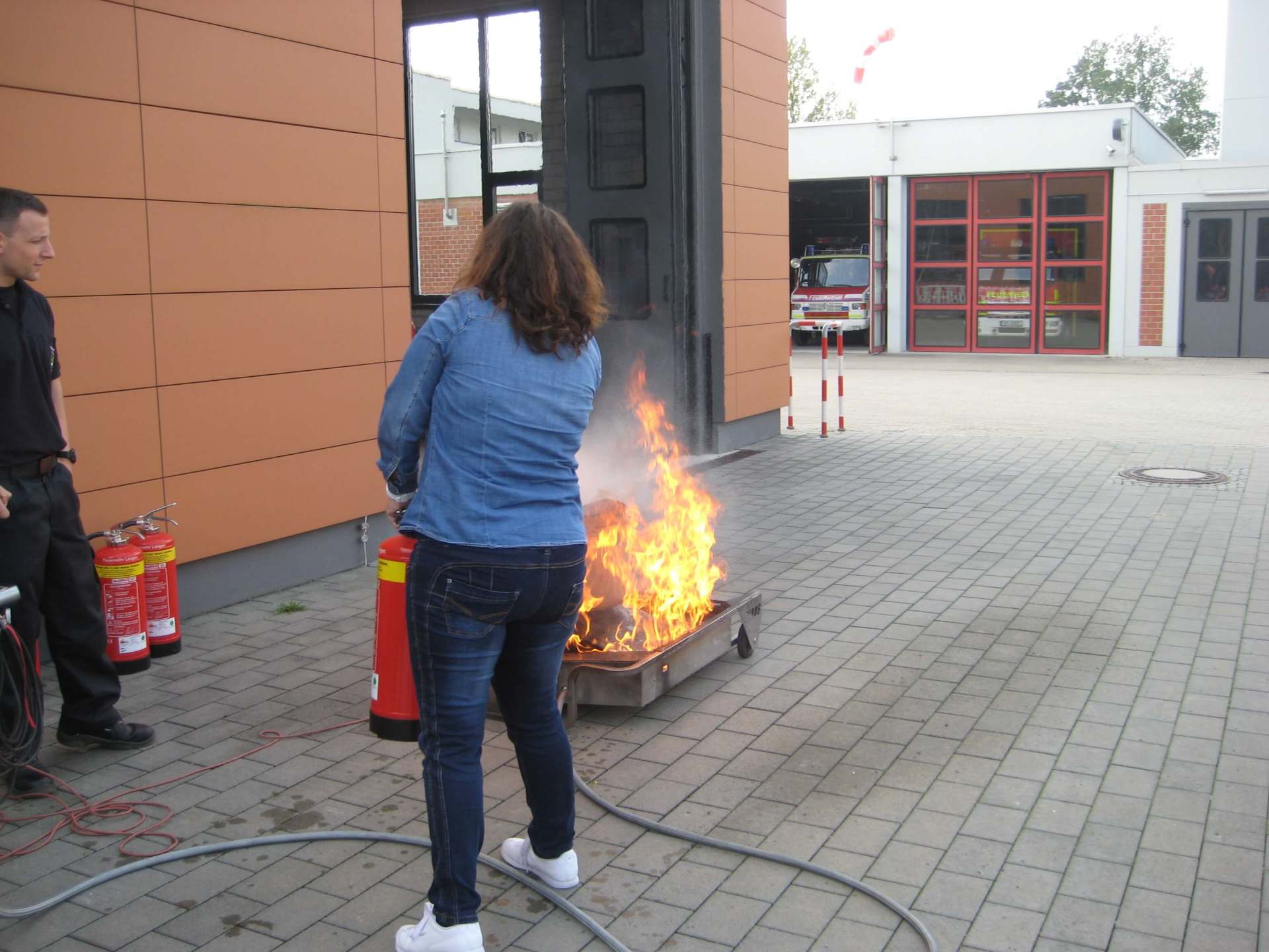 Menschen in der Nähe eines kleinen Feuers im Freien, das in einer Metallschale neben einem Gebäude brennt.