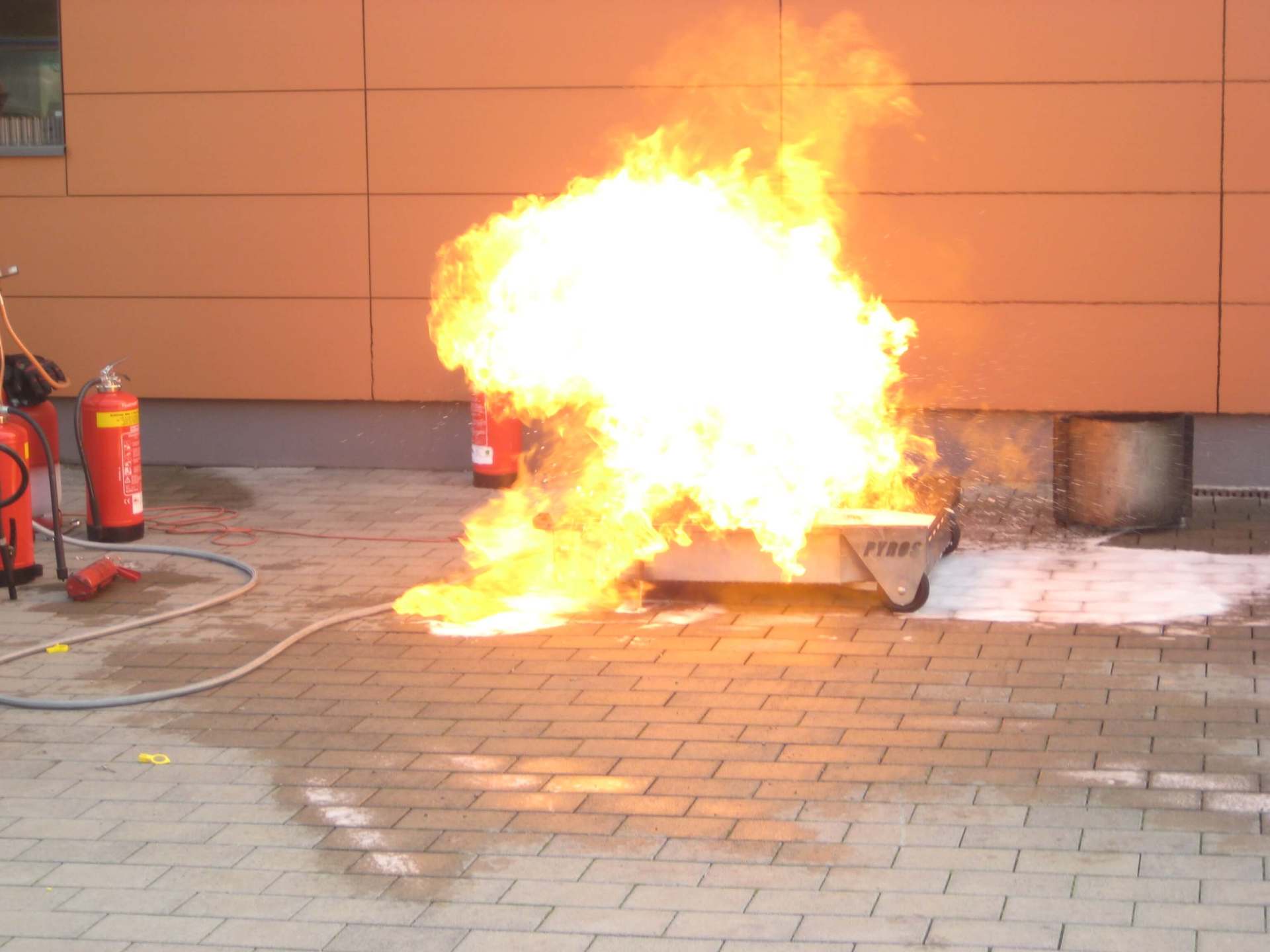 Kleiner Brand oder Explosion auf dem Gehweg in der Nähe einer Mauer, ein Feuerlöscher ist in der Nähe.