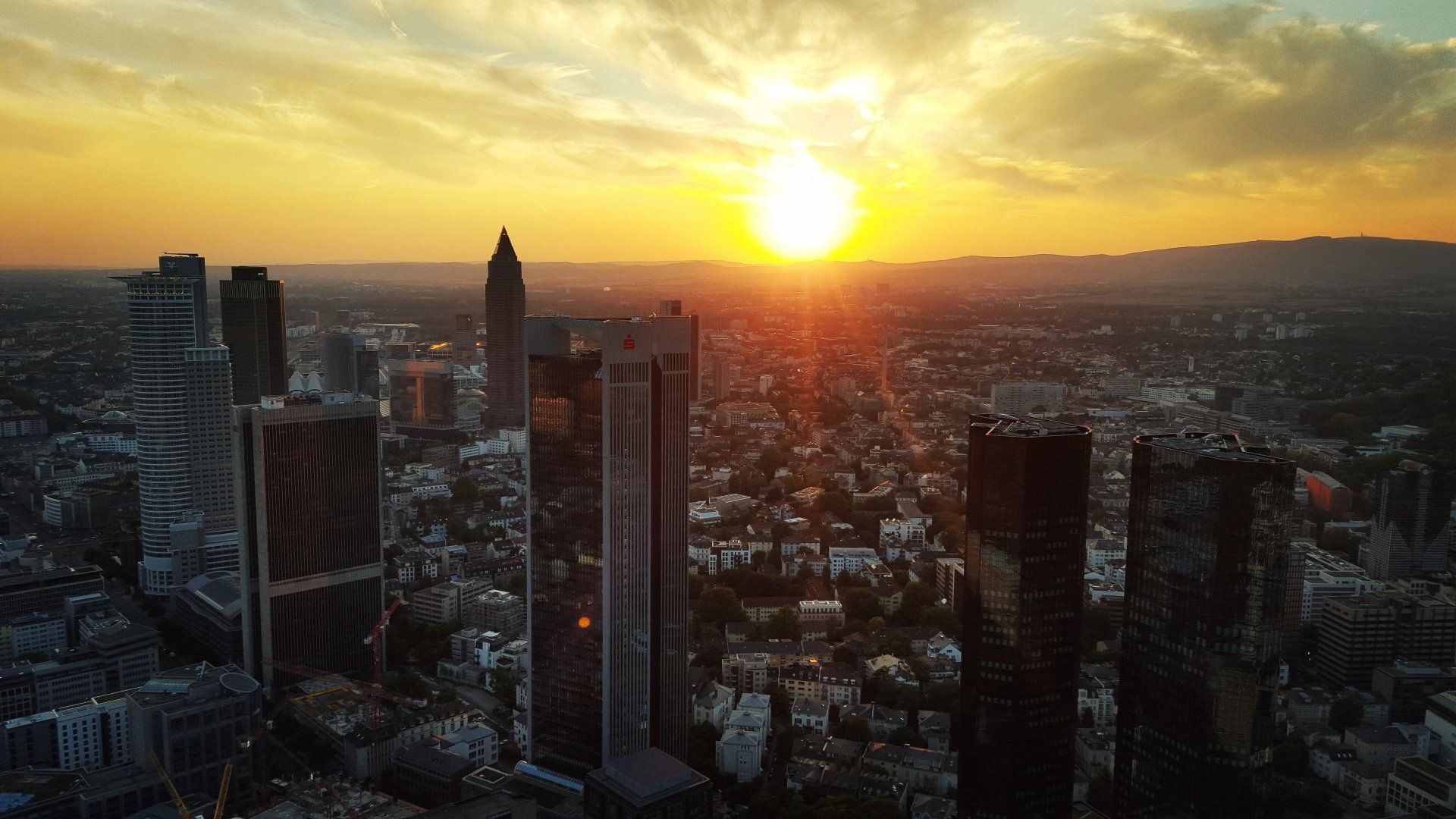Sonnenuntergang über der Skyline einer Stadt, deren hohe Gebäude sich vor einem leuchtend orangefarbenen Himmel abzeichnen.