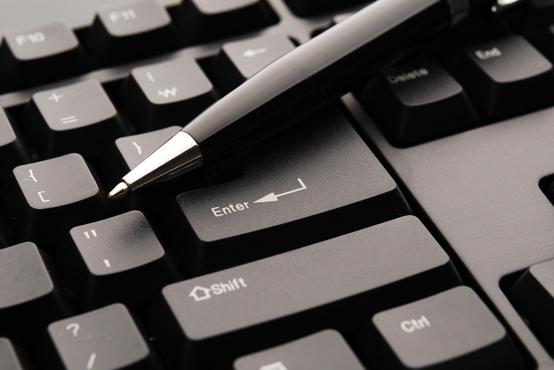 Nahaufnahme eines Stiftes, der auf den Tasten einer Laptop-Tastatur mit den Bezeichnungen „E-Mail“ und „Start“ schreibt.