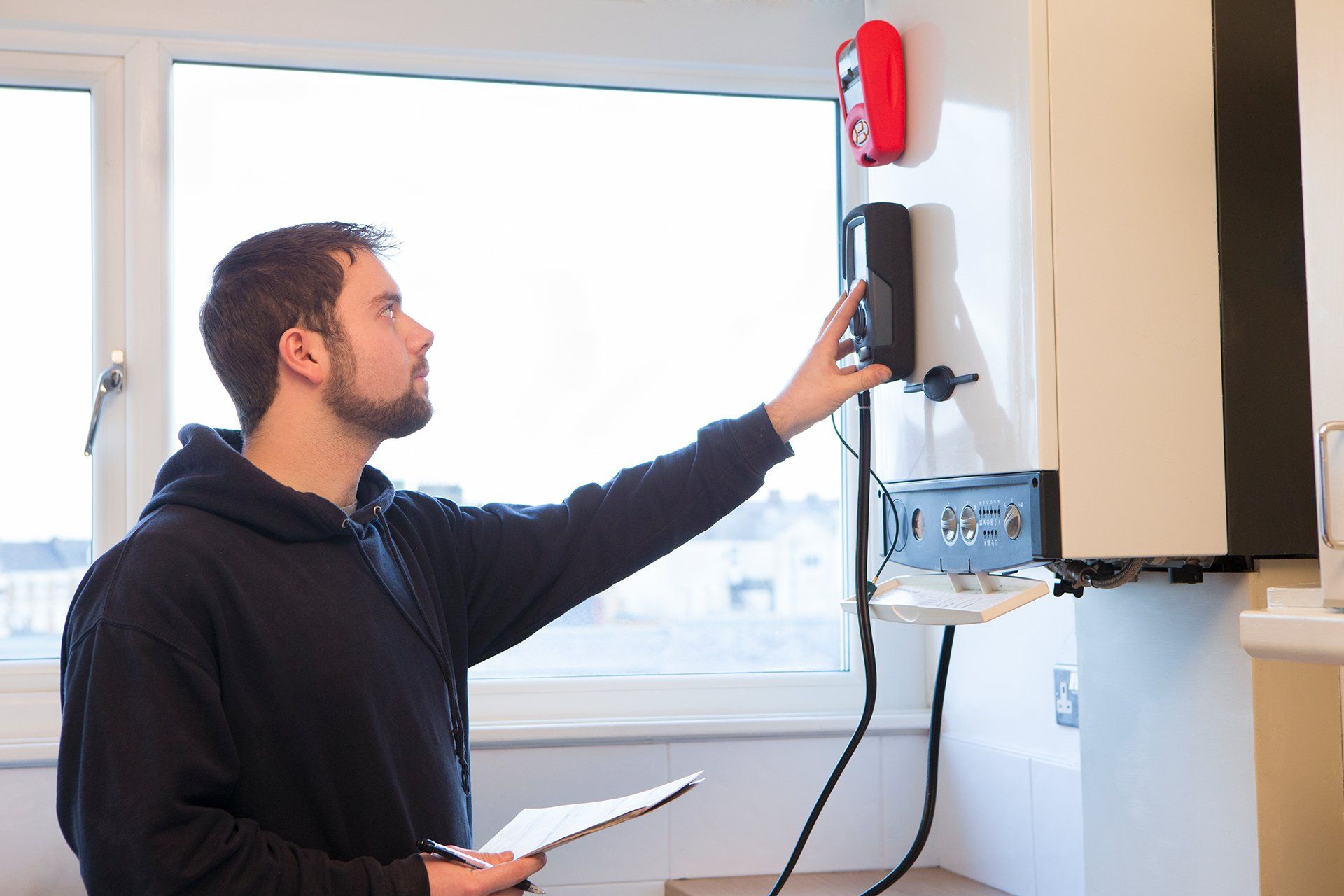 A man is looking at a device on a wall while holding a clipboard.