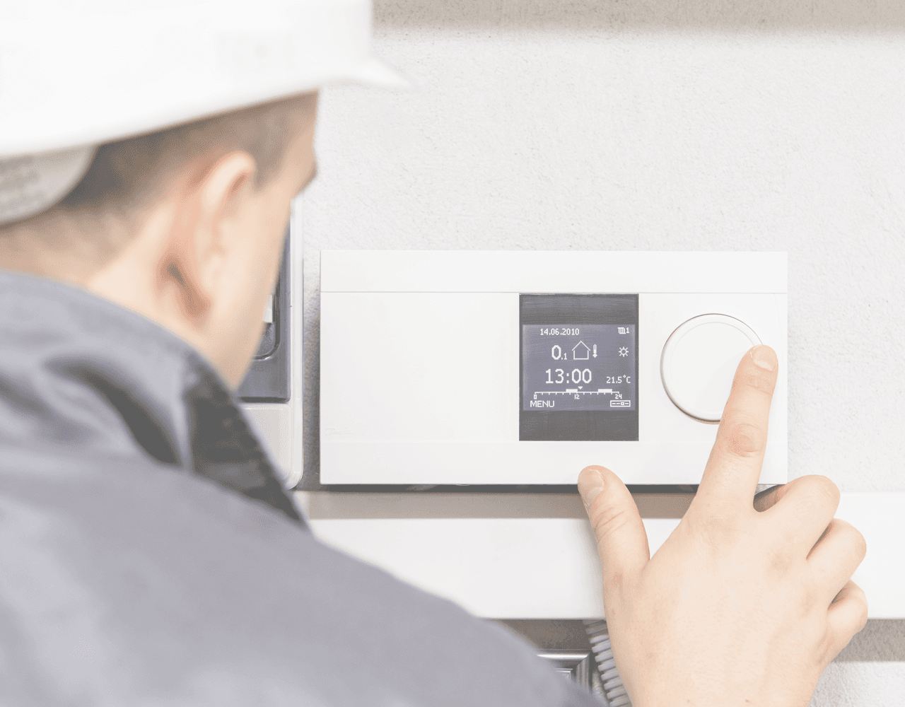 A man is adjusting a thermostat on a wall.