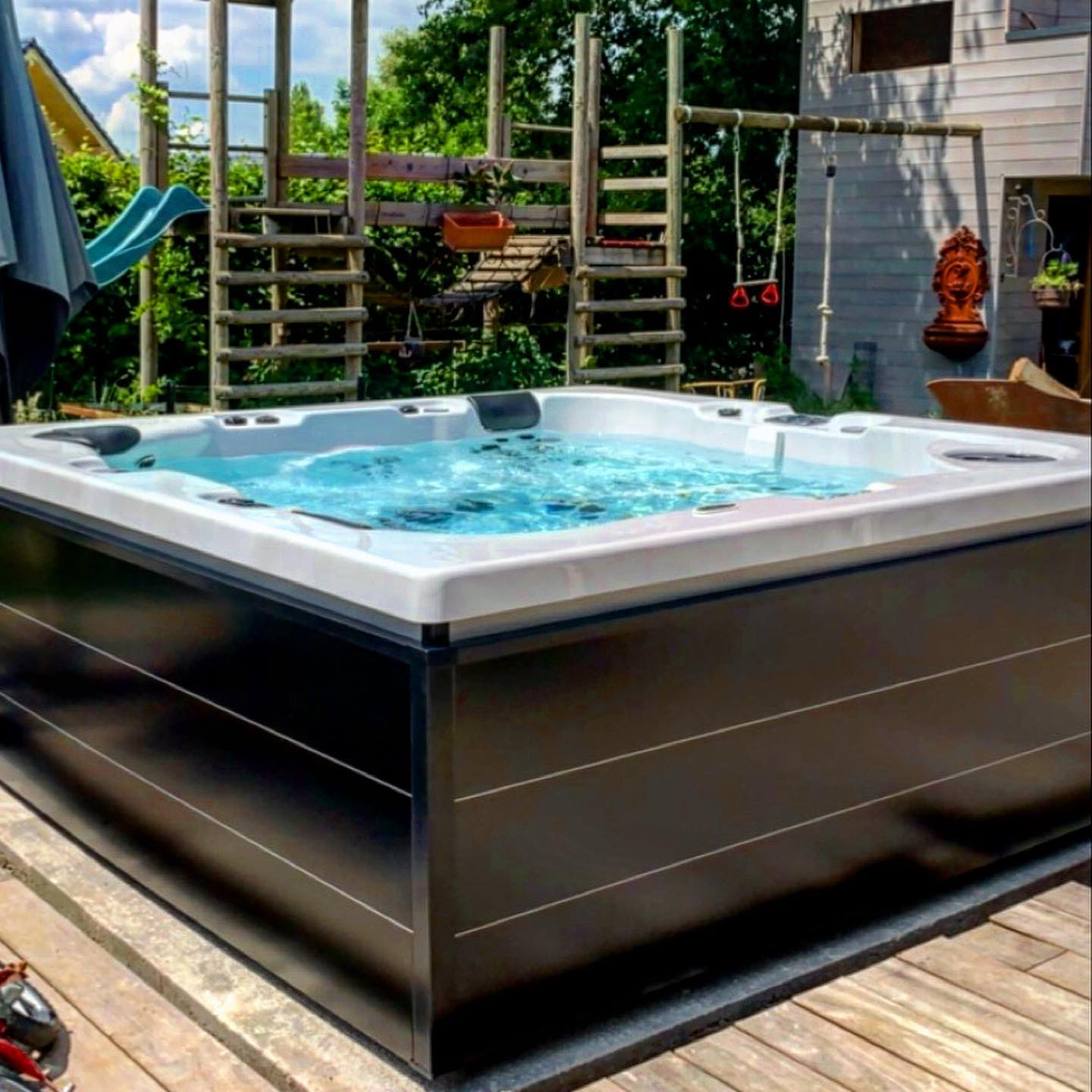 Un bain à remous est installé sur une terrasse en bois devant une aire de jeux.