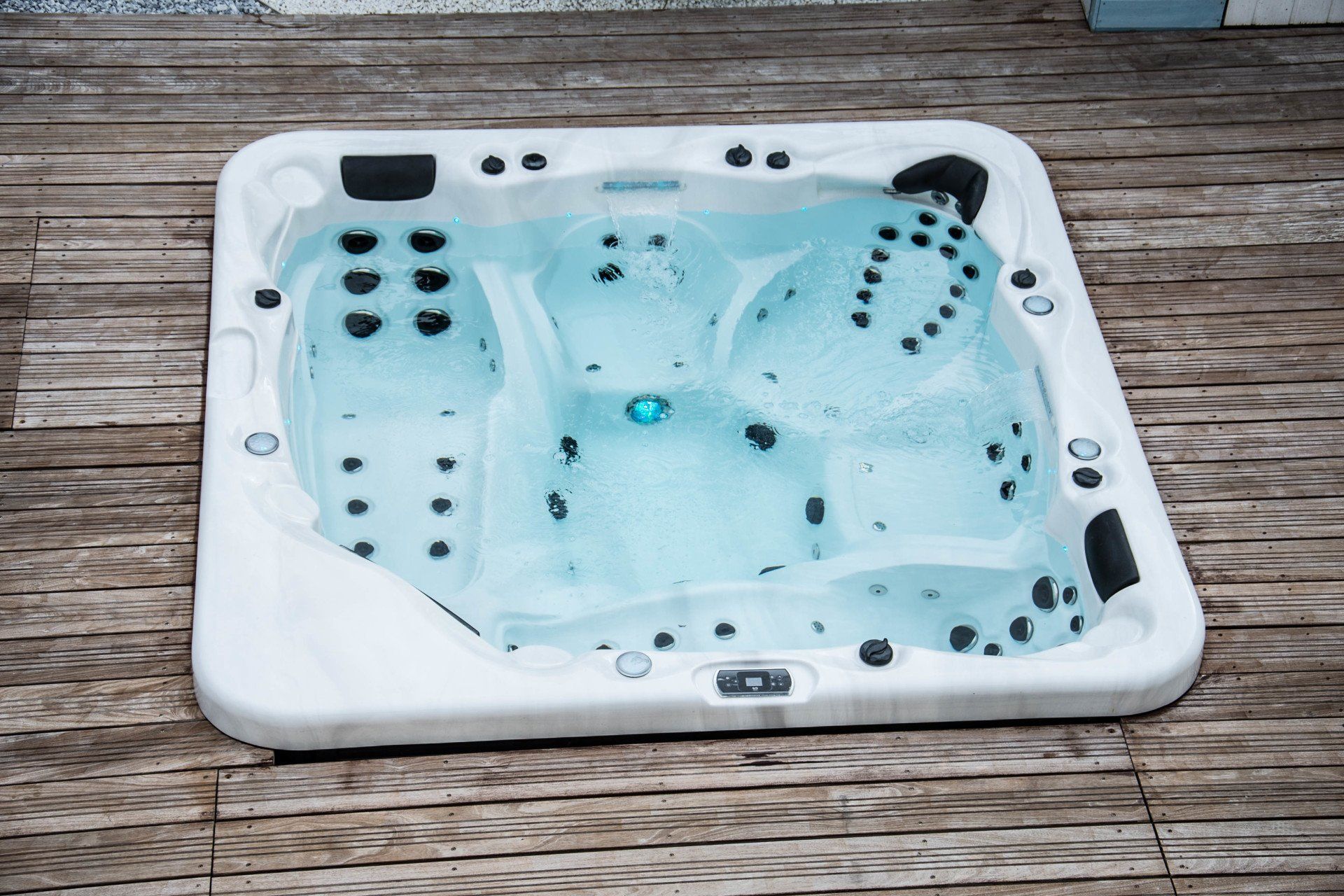 Un bain à remous blanc avec de l'eau bleue est posé sur une terrasse en bois.