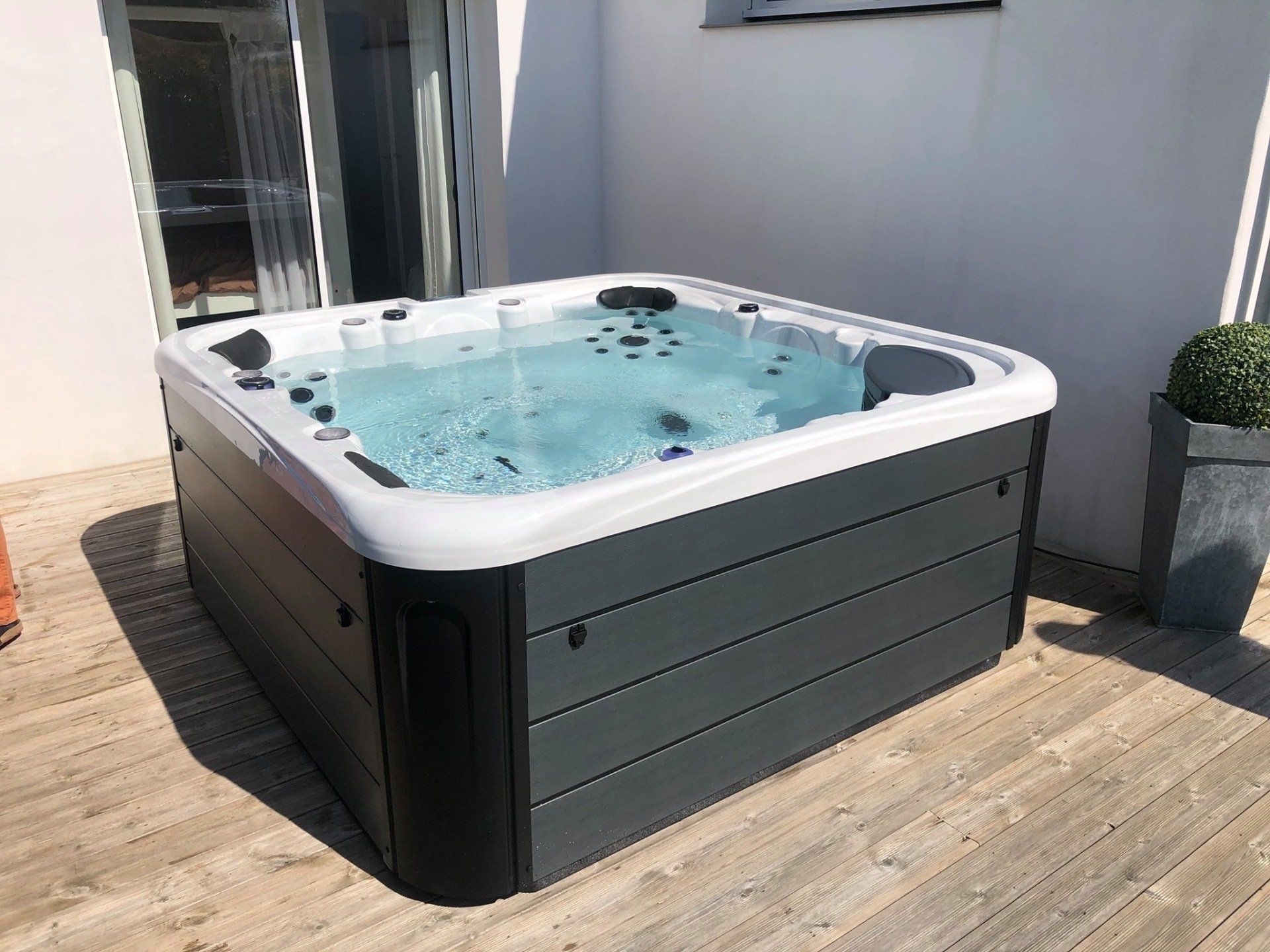 Un bain à remous est installé sur une terrasse en bois à côté d'un bâtiment.