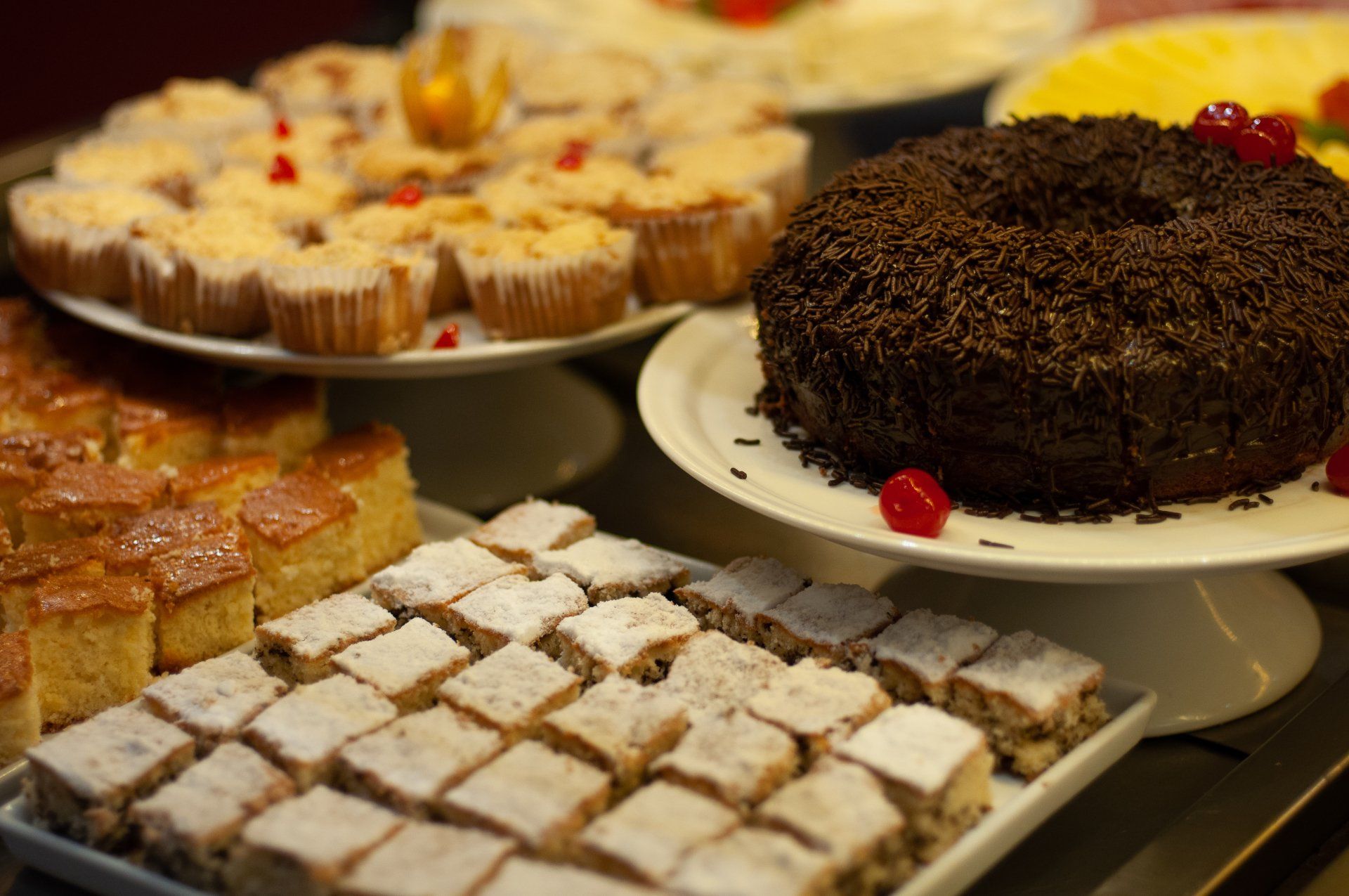 Variedade de produtos assados em pratos: muffins, bolo com granulado, quadradinhos com açúcar de confeiteiro.