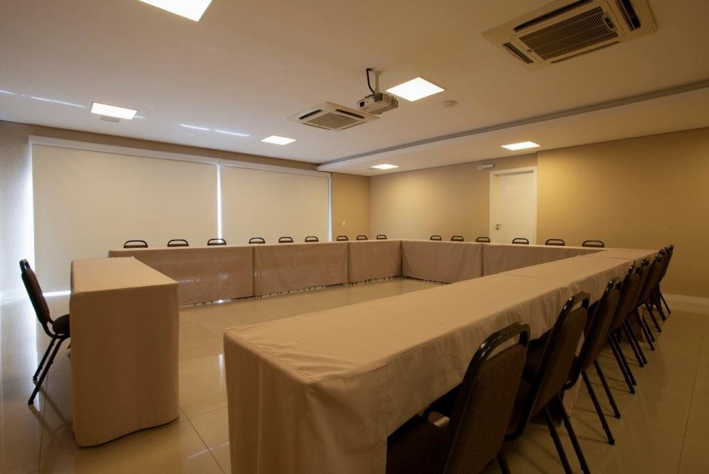 Sala de conferências com mesa em U, cadeiras, projetor, cores neutras.