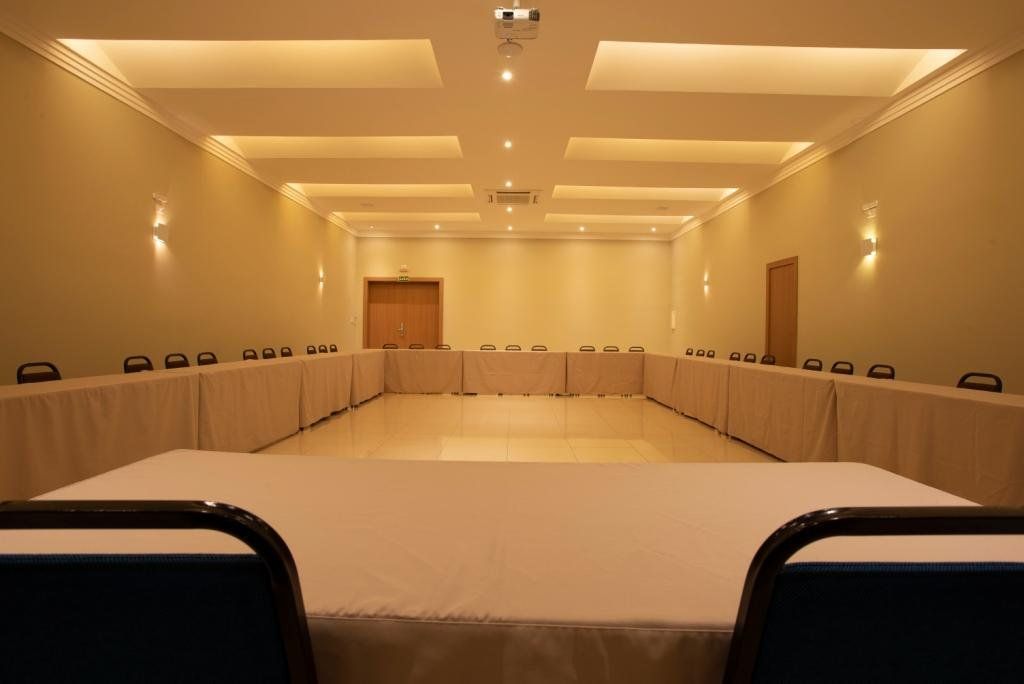 Sala de conferências com mesa em formato de U, cadeiras e iluminação suspensa.