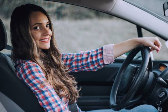 Giovane donna  sorridente alla guida in auto
