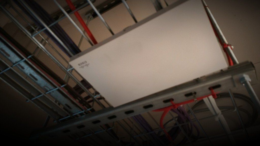 Ceiling-mounted metal panel with exposed cables and red wiring in an industrial interior