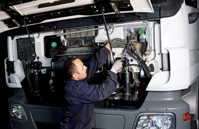Mechanic working on the engine of a truck with the hood open.