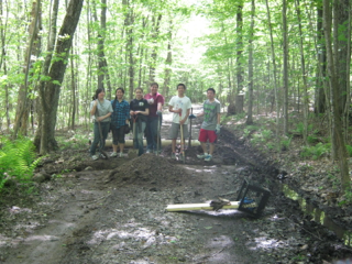 A group of people standing next to a pile of dirt in the woods.