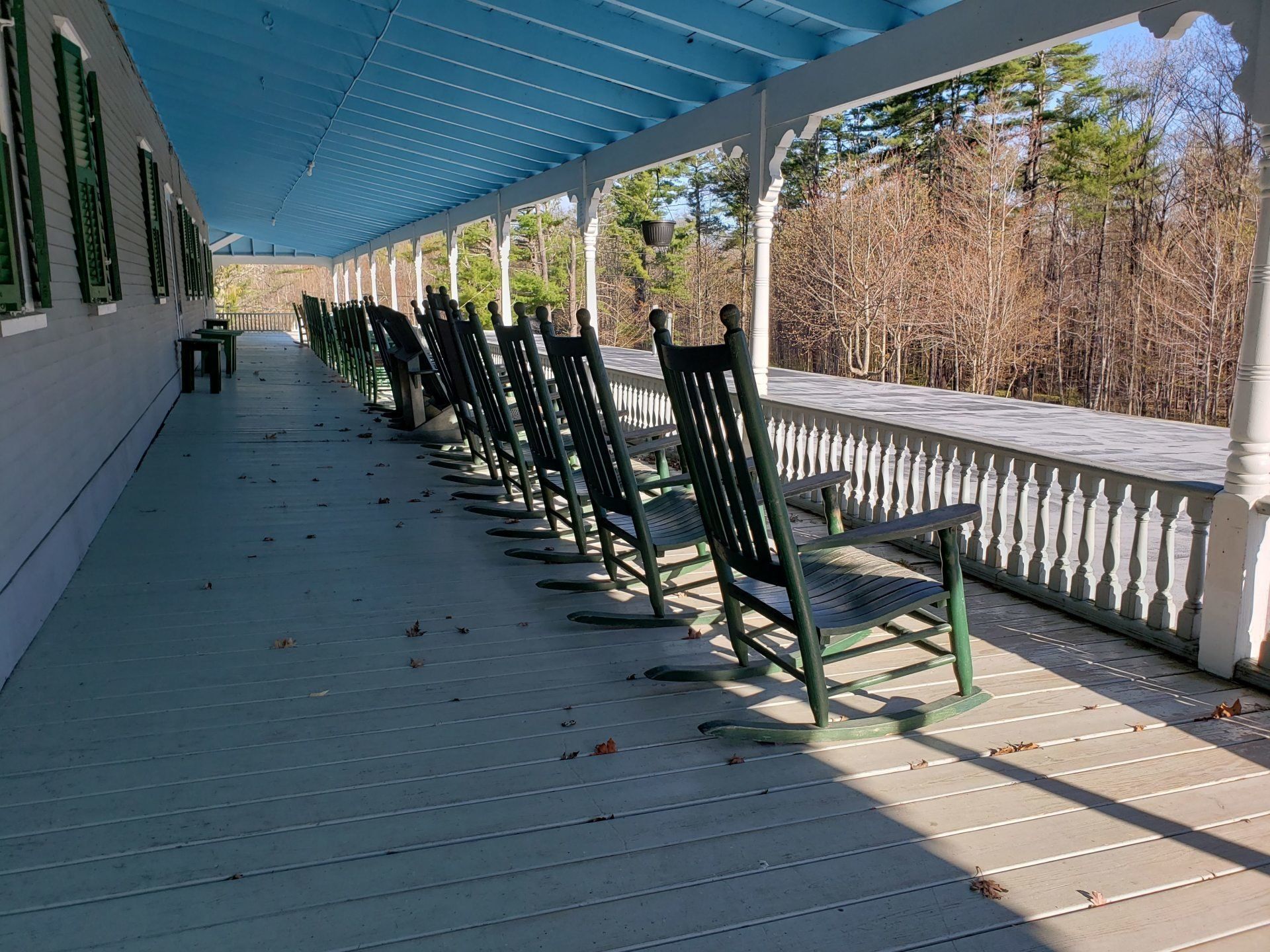 A row of rocking chairs on a porch with a blue roof.