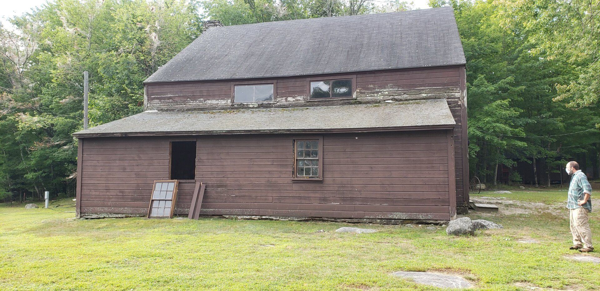 A man is standing in front of an old wooden house.