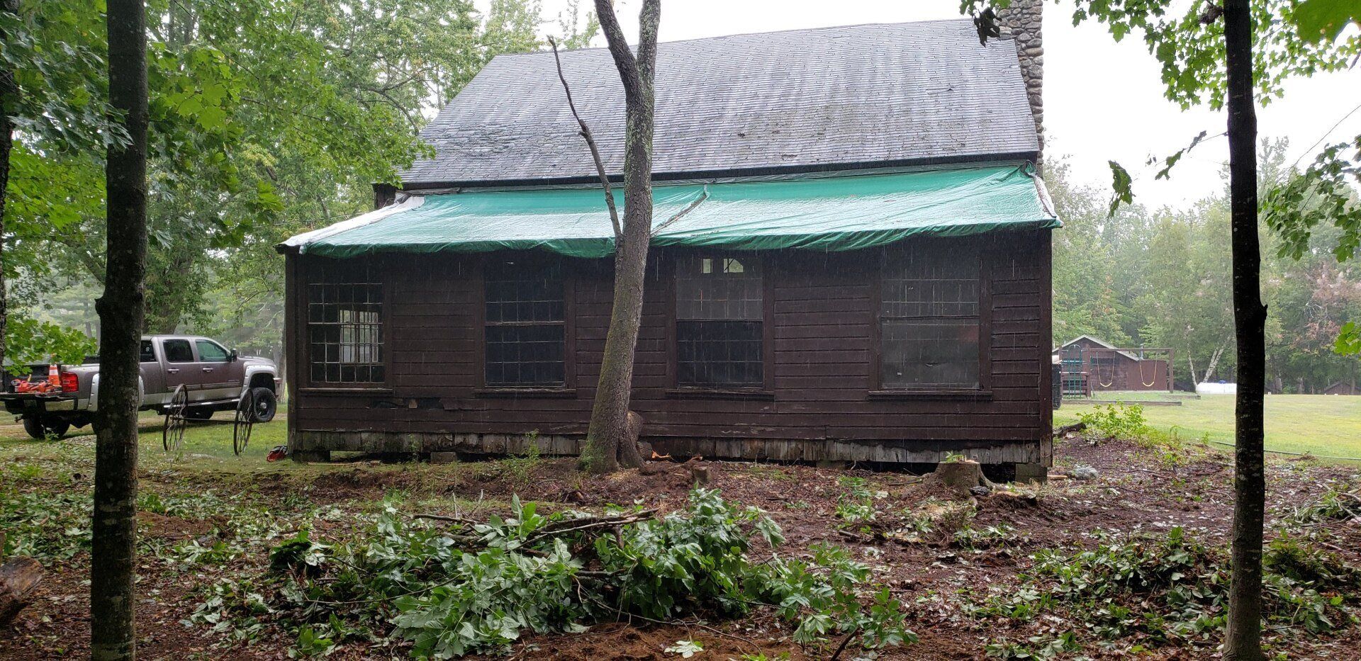 A log cabin with a green tarp on the roof is sitting in the middle of a forest.