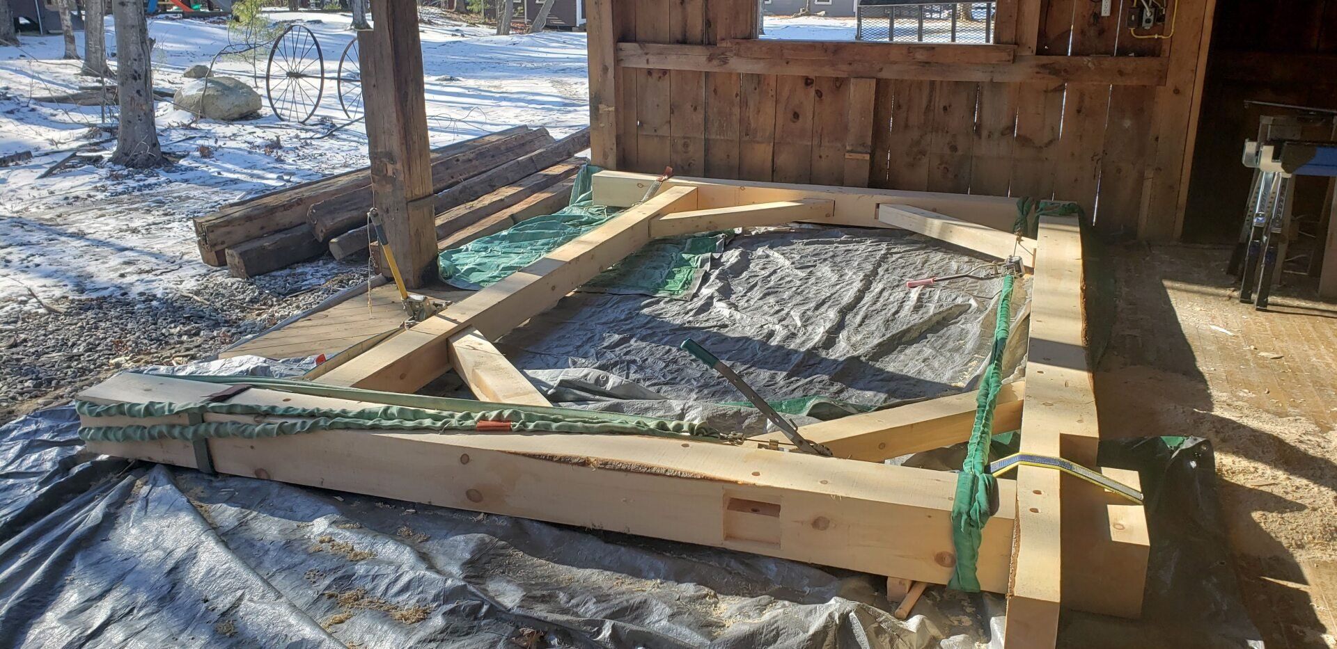 A wooden structure is sitting on top of a tarp in front of a wooden building.