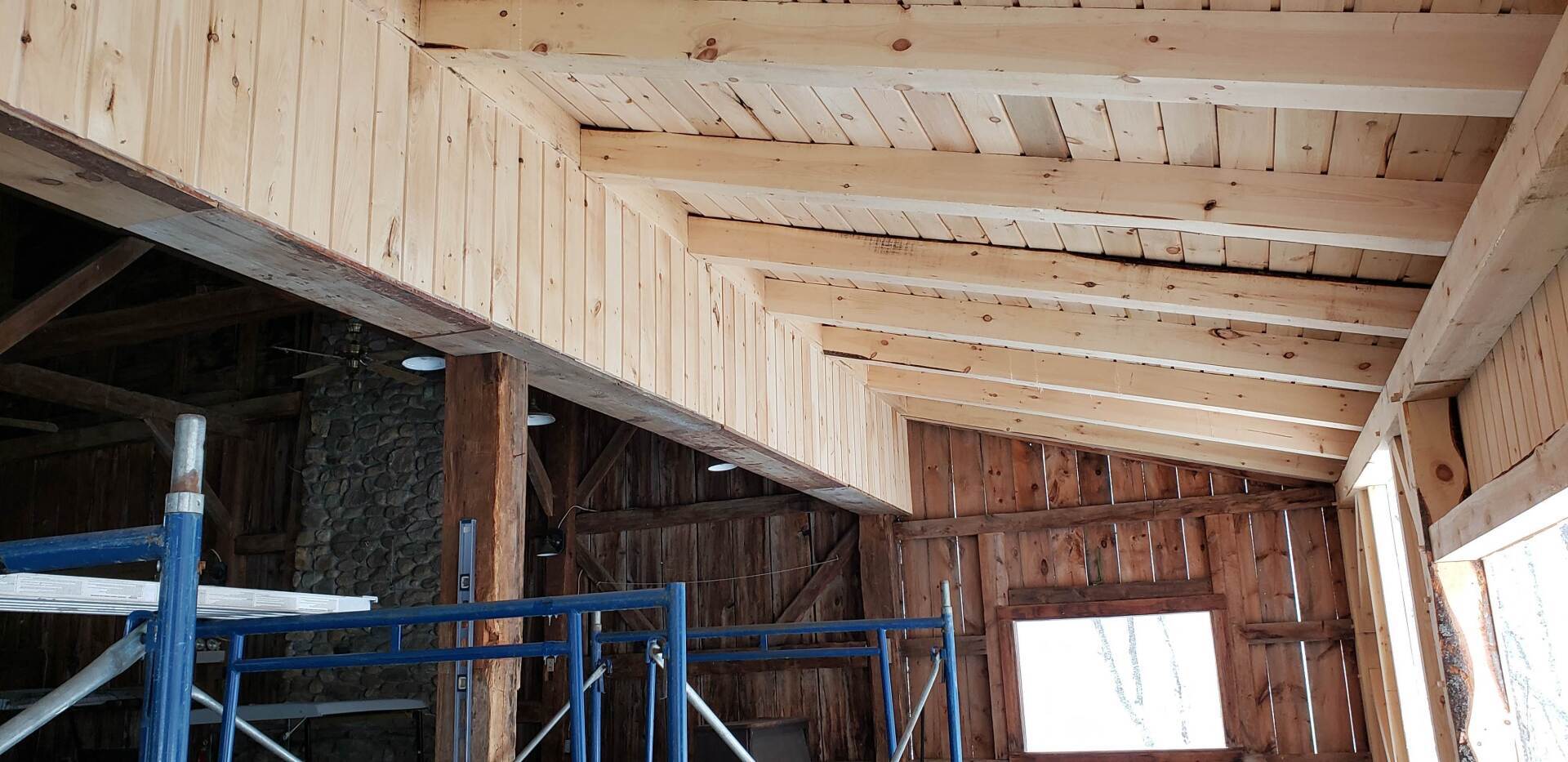 The inside of a barn under construction with wooden beams and scaffolding.