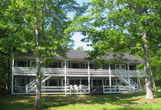 A large white house with a black roof is surrounded by trees.