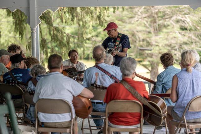 A group of people are sitting in chairs under a tent while a man plays a guitar.