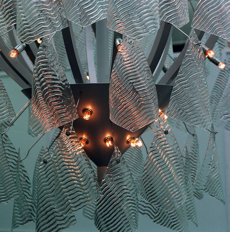 Abstrakte Metallskulptur mit gewellten silbernen Bändern und leuchtend orangefarbenen Lichtern in der Mitte