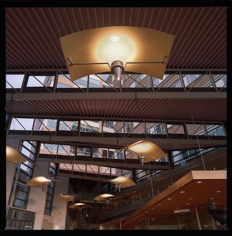 Modernes Atrium im Innenbereich mit Oberlichtern, Stahlträgern und hängenden goldenen Leuchten