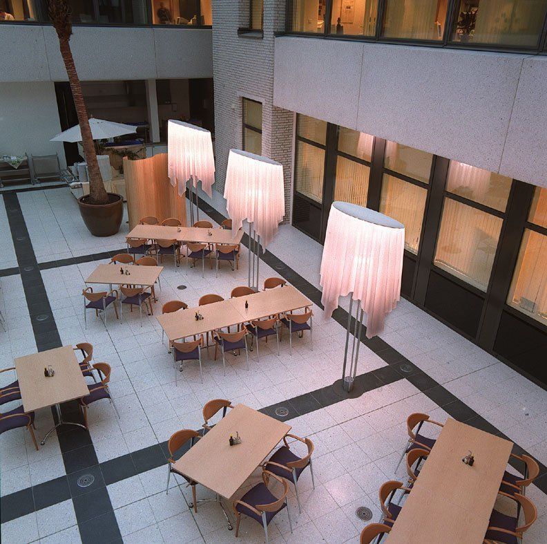 Moderner Atrium-Essbereich mit leeren Tischen, Stühlen und hohen rosa Lampen unter den Fenstern.