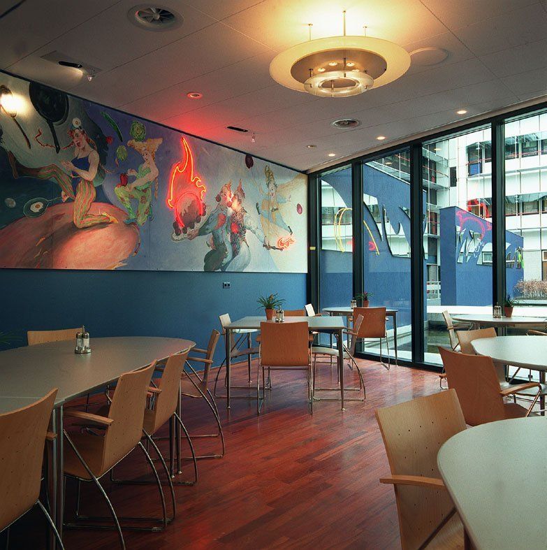 Farbenfrohes Café-Interieur mit Tischen, Stühlen, Wandmalereien und großen Fenstern mit Blick auf eine Straße