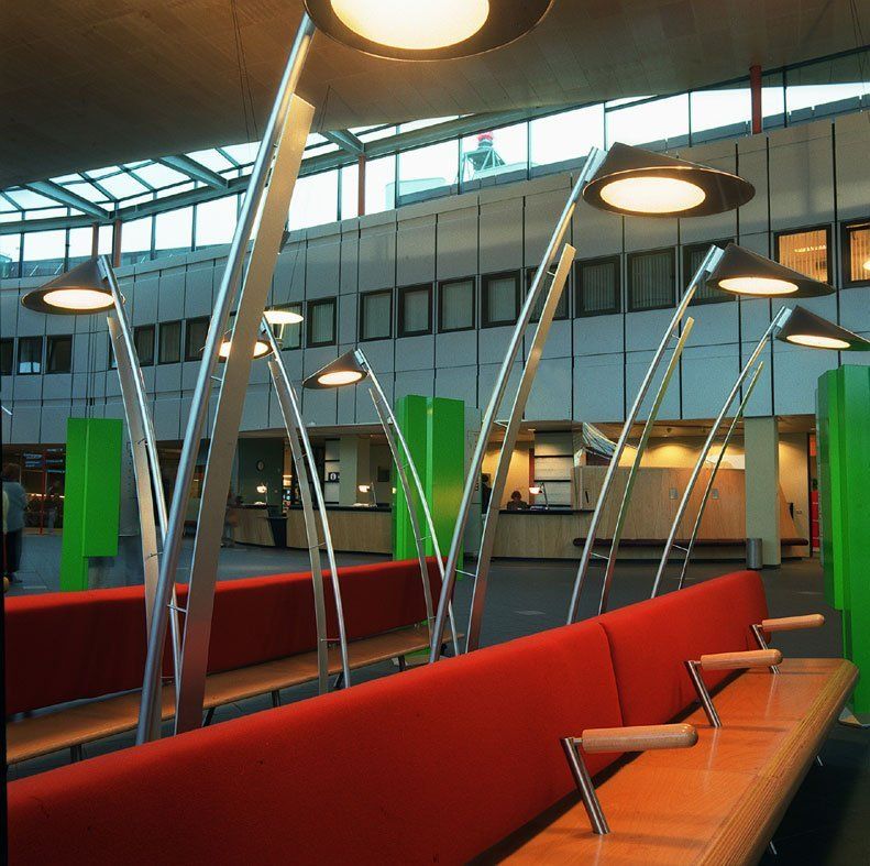 Modernes Büro-Atrium mit roten Sitzmöbeln, Holztischen und hohen, schrägen Leuchten.