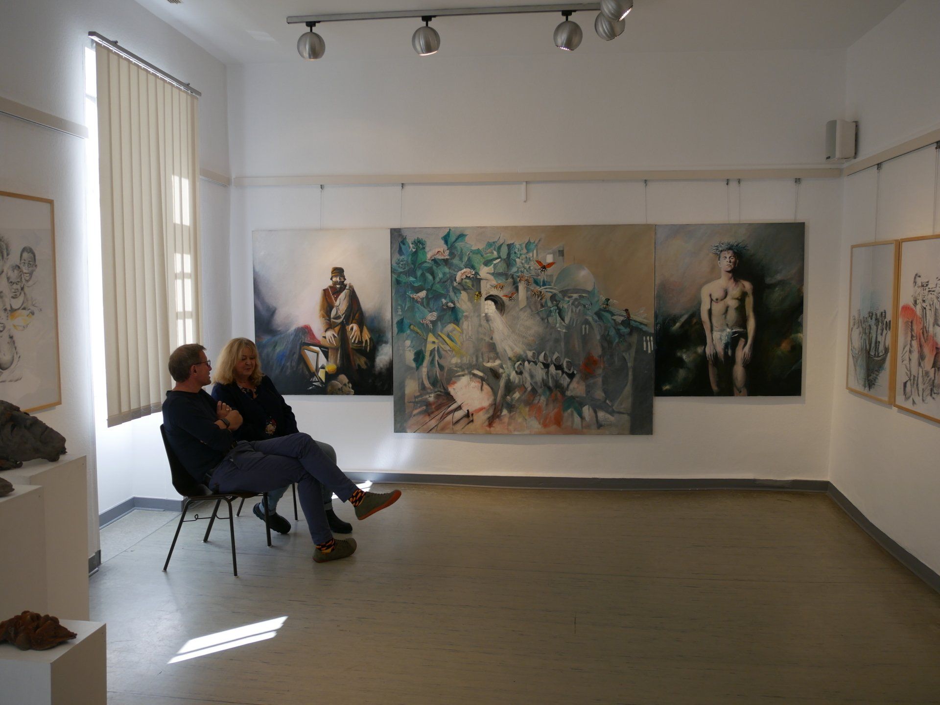 Kunstgalerie mit großen abstrakten Gemälden an weißen Wänden und zwei im Vordergrund sitzenden Personen.