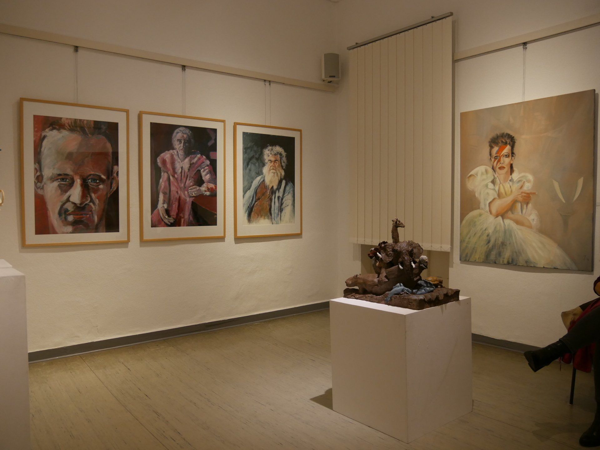 Kunstgalerie mit gerahmten Porträts an cremefarbenen Wänden und einer Skulptur auf einem weißen Sockel.