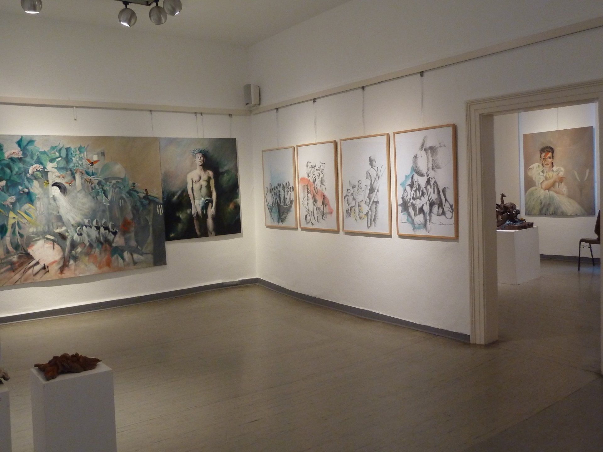 Ein Ausstellungsraum mit abstrakten Gemälden an weißen Wänden und einem Durchgang zu einer weiteren Ausstellung.