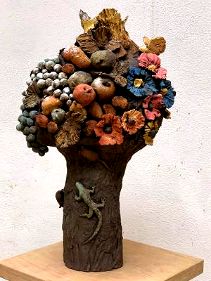 Kleine, dekorative Baumskulptur mit strukturiertem Stamm und farbenfroher Blüten- und Kieselkrone auf einem Holzsockel
