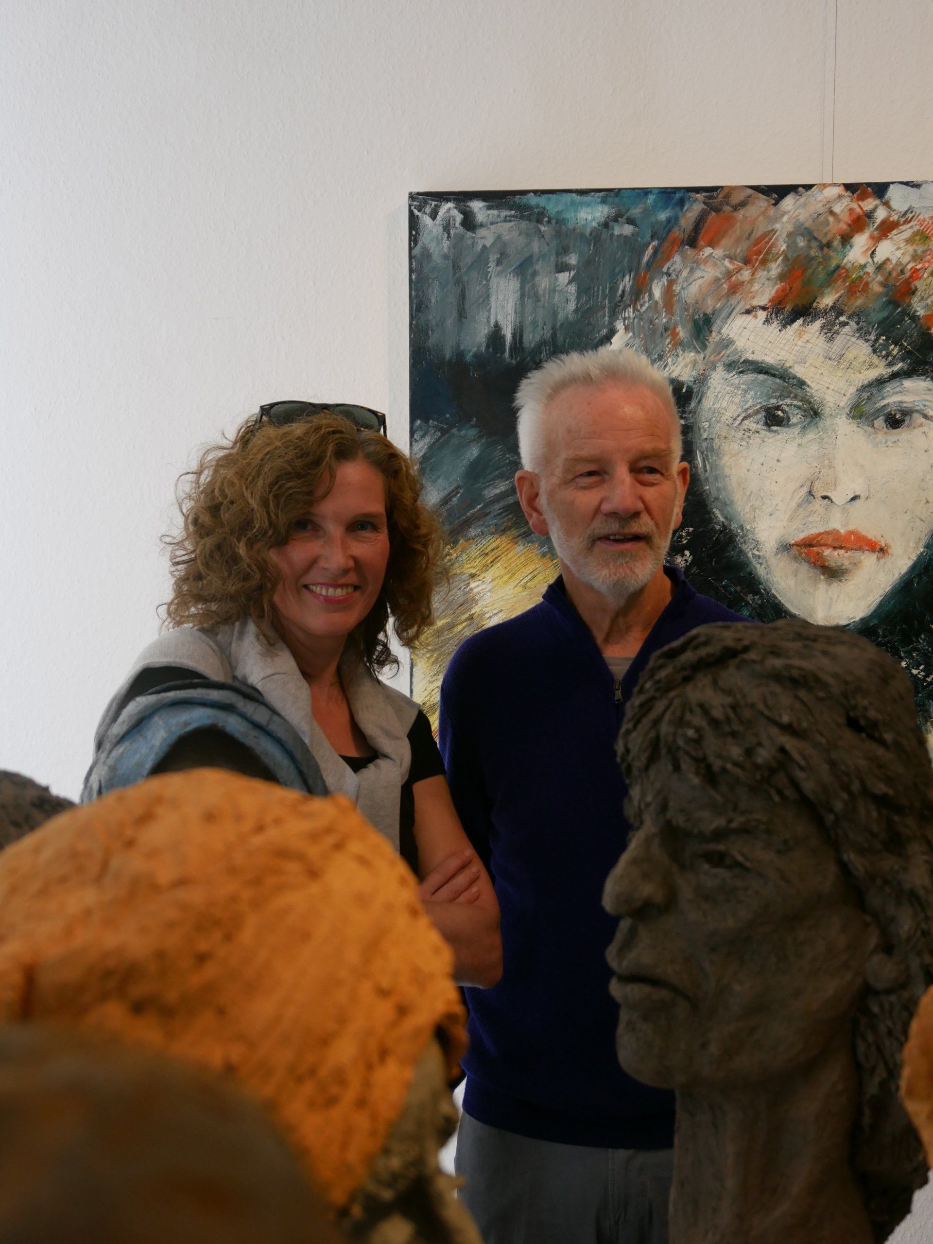 Zwei Personen posieren neben gemalten Porträts in einer Galerie