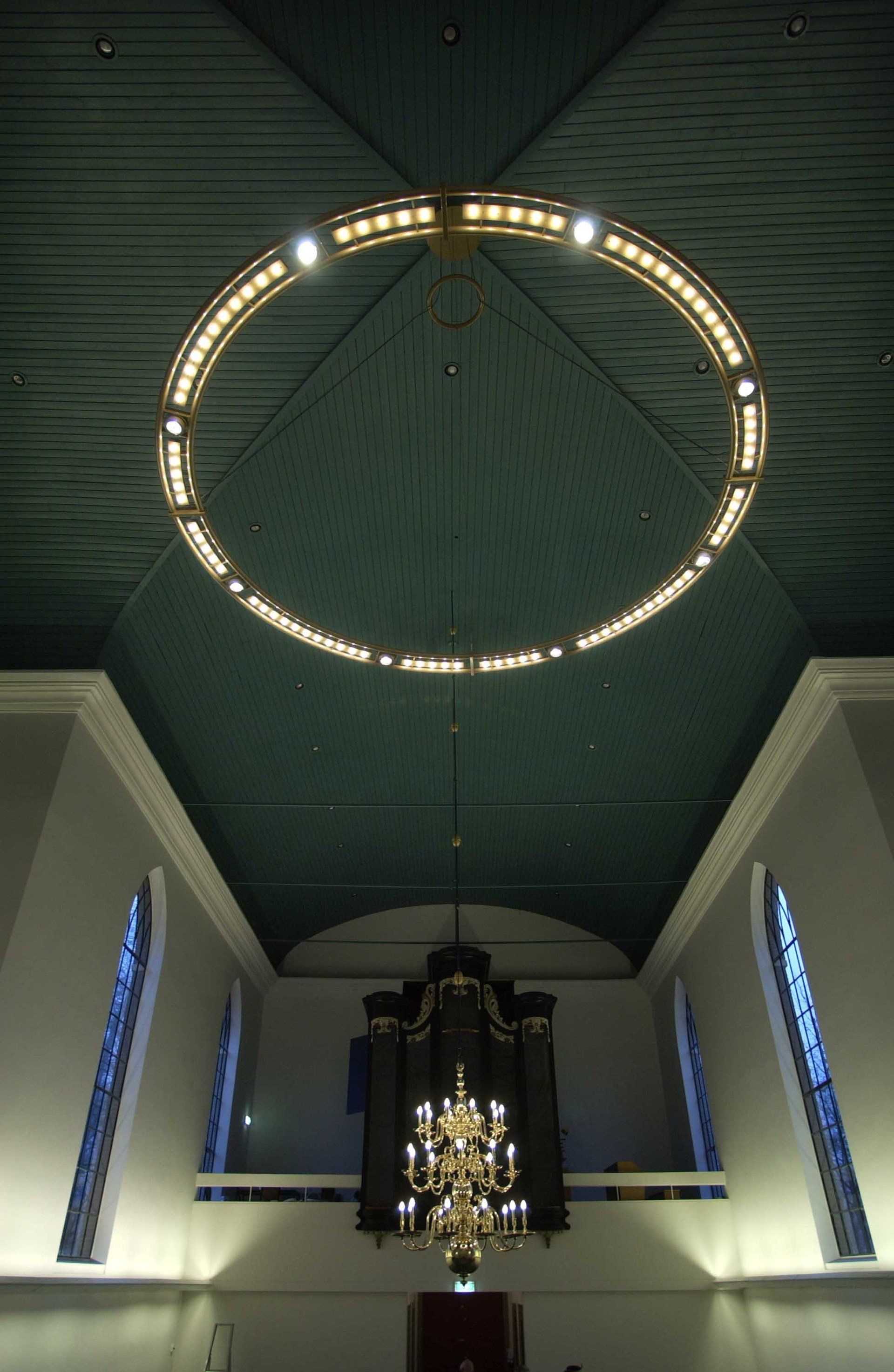 Ein runder Kronleuchter hängt von der hohen Gewölbedecke im Inneren einer Kirche herab.