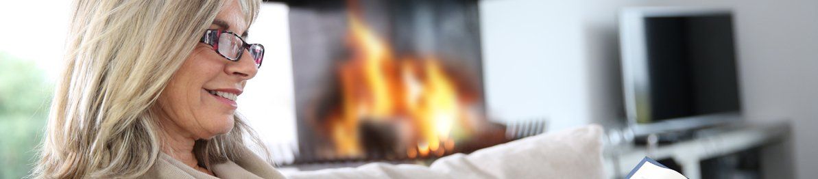 Older lady wearing glasses, reading a book by the fire