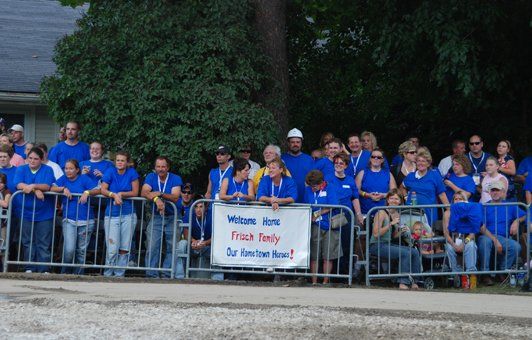 Crowd wearing blue shirts behind metal barriers, holding a 