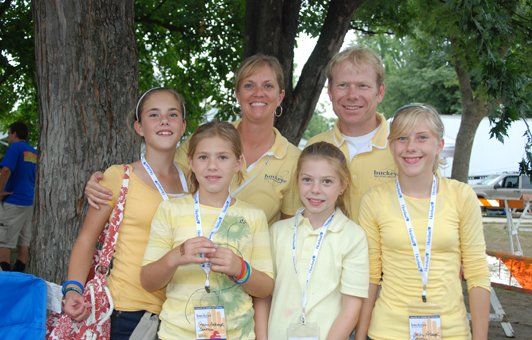Family of six in yellow shirts, smiling, standing outside near a tree.