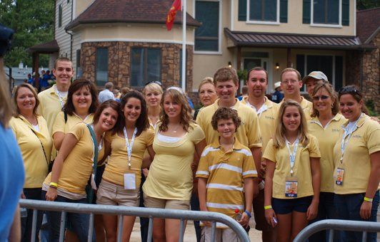 Group of people wearing yellow shirts posing near a building with an American flag.