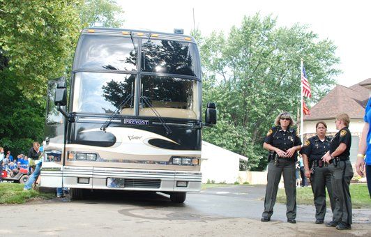 Three uniformed law enforcement officers standing near a luxury bus parked on a street.
