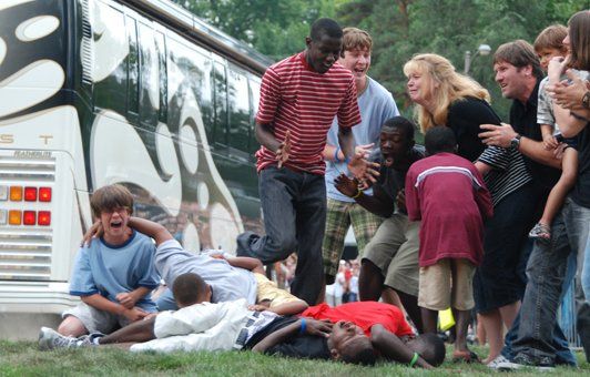 People gathered near a bus, some laughing, others on the ground, possibly staged or a game.