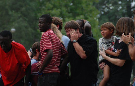 Group of people outdoors: one in red shirt, another in striped shirt, a child is held, some looking at camera.