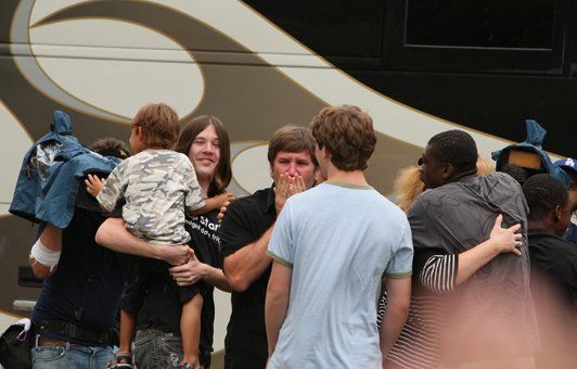 People embracing near a bus; one person is covering their face, others have arms around them.