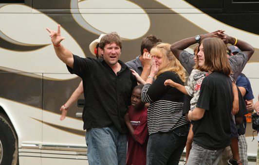 Group of people near a bus, some smiling and waving, in an outdoor setting.