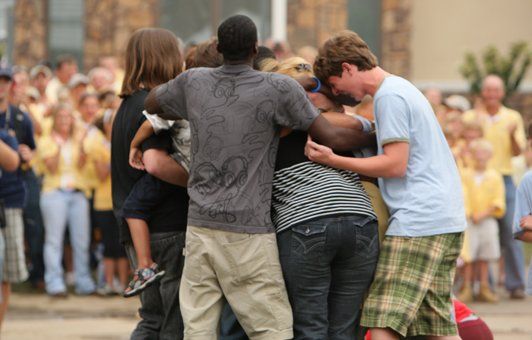 Group of people in a tight hug, surrounded by a crowd.