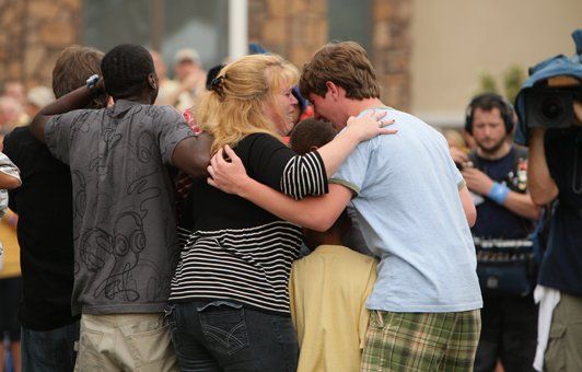 Group of people embracing outdoors; likely a moment of comfort and support.