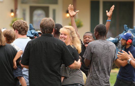 People cheering excitedly in front of a house, some with arms raised.