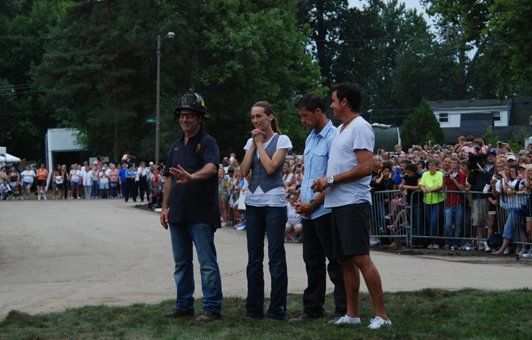 The man in the front gestures with a helmet. Others stand with hands clasped.